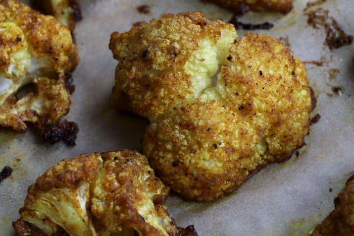 Close up photo of pieces of curried cauliflower on parchment paper on baking sheet