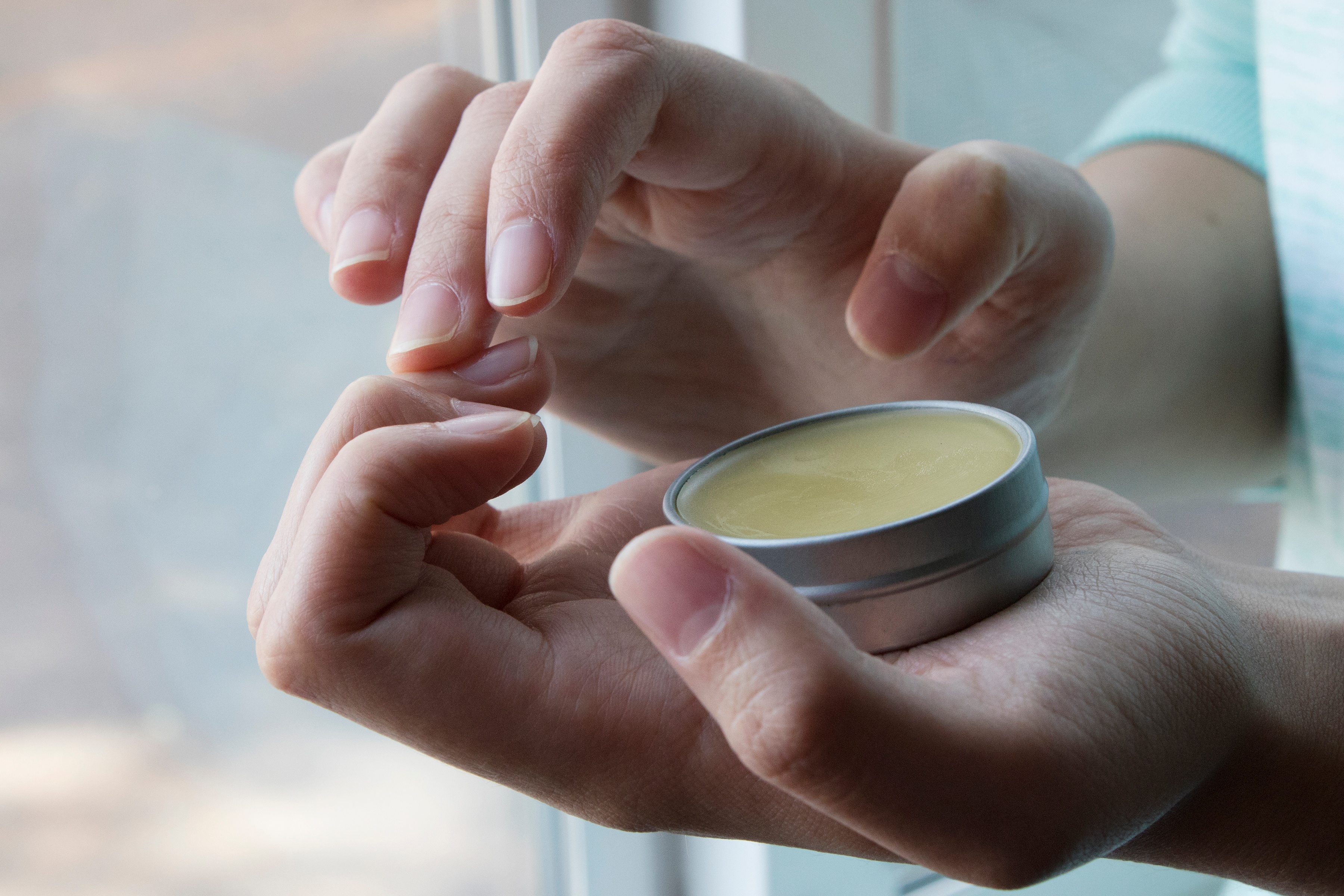 Natural looking hands holding tin of salve and rubbing fingernails
