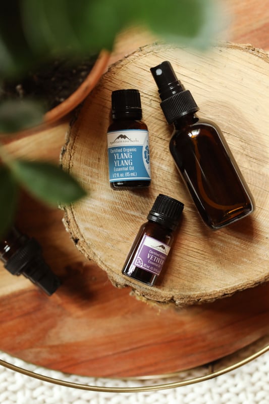 Bottles of organic essential oils from Mountain Rose Herbs on wooden round with glass spritzer bottle.