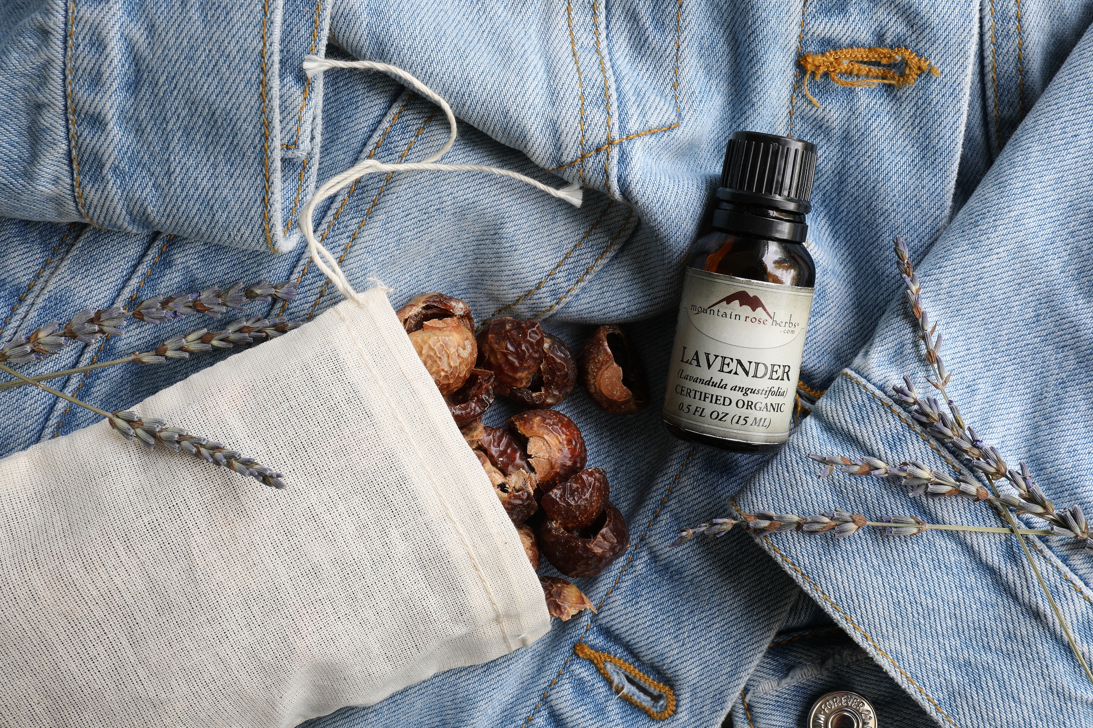 Soap nuts in muslin bag laying on jeans next to lavender essential oil and flowers