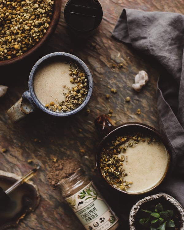 Cups of tea with loose chamomile flowers and a bottle of spices. 