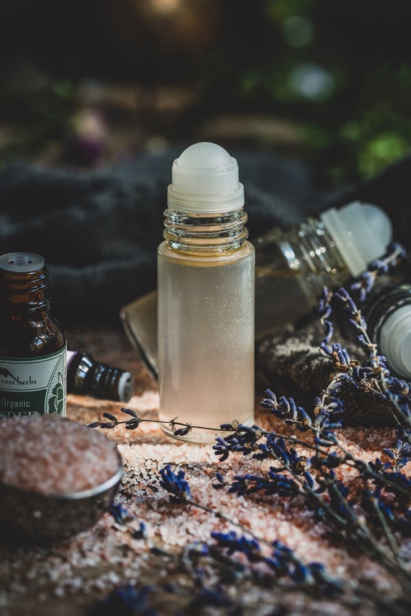 Homemade deodorant in a glass roll top bottle, surrounded by pink sea salt and dried lavender flowers.