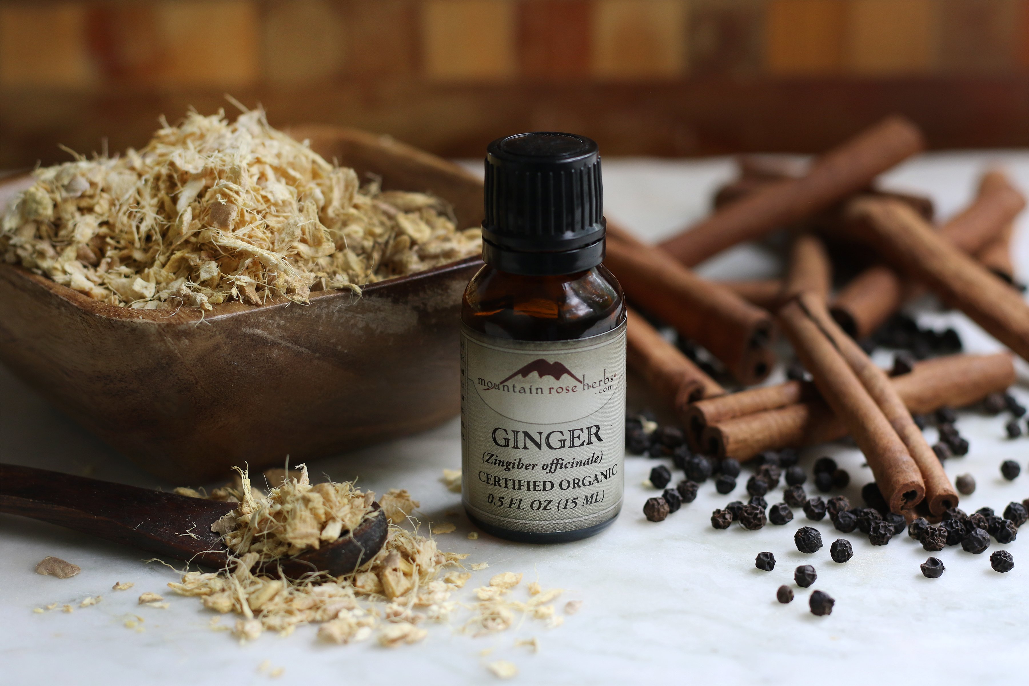 Organic and fair trade ginger essential oil arranged with dried and cut ginger root, organic cinnamon sticks and peppercorns. 