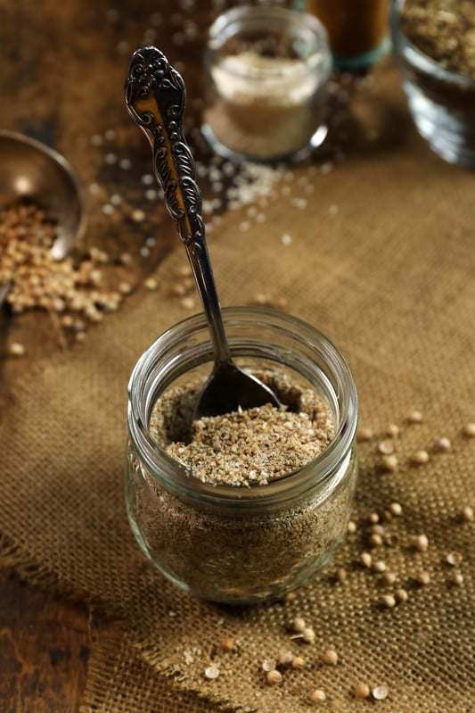 Dukkah spice nut and seed blend in glass jar with spoon.