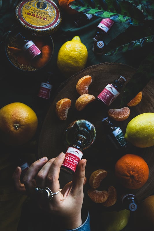 Hand dropping essential oils into bottle surrounded by fresh and vibrant ingredients. 