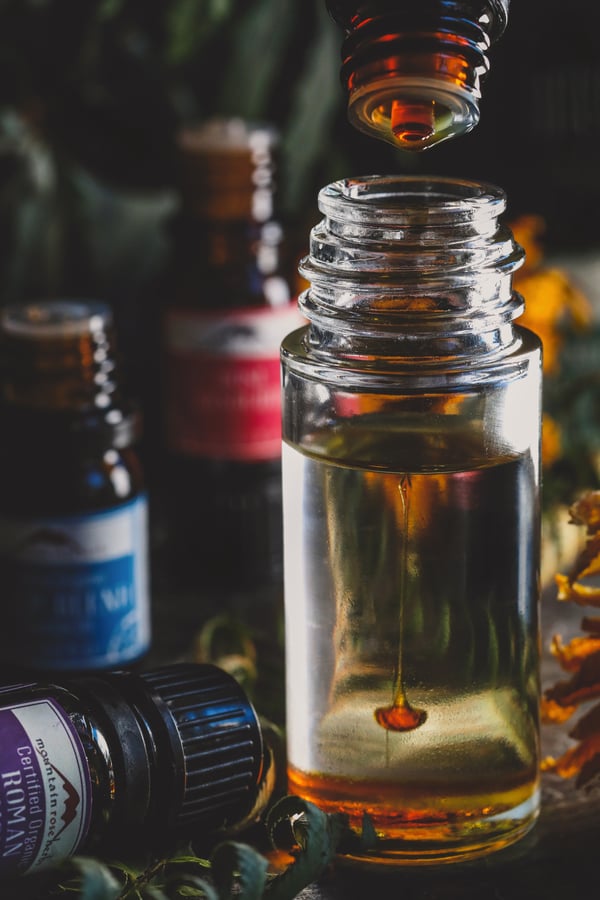 Clear glass bottle of oil with colorful essential oil dropping into it. 