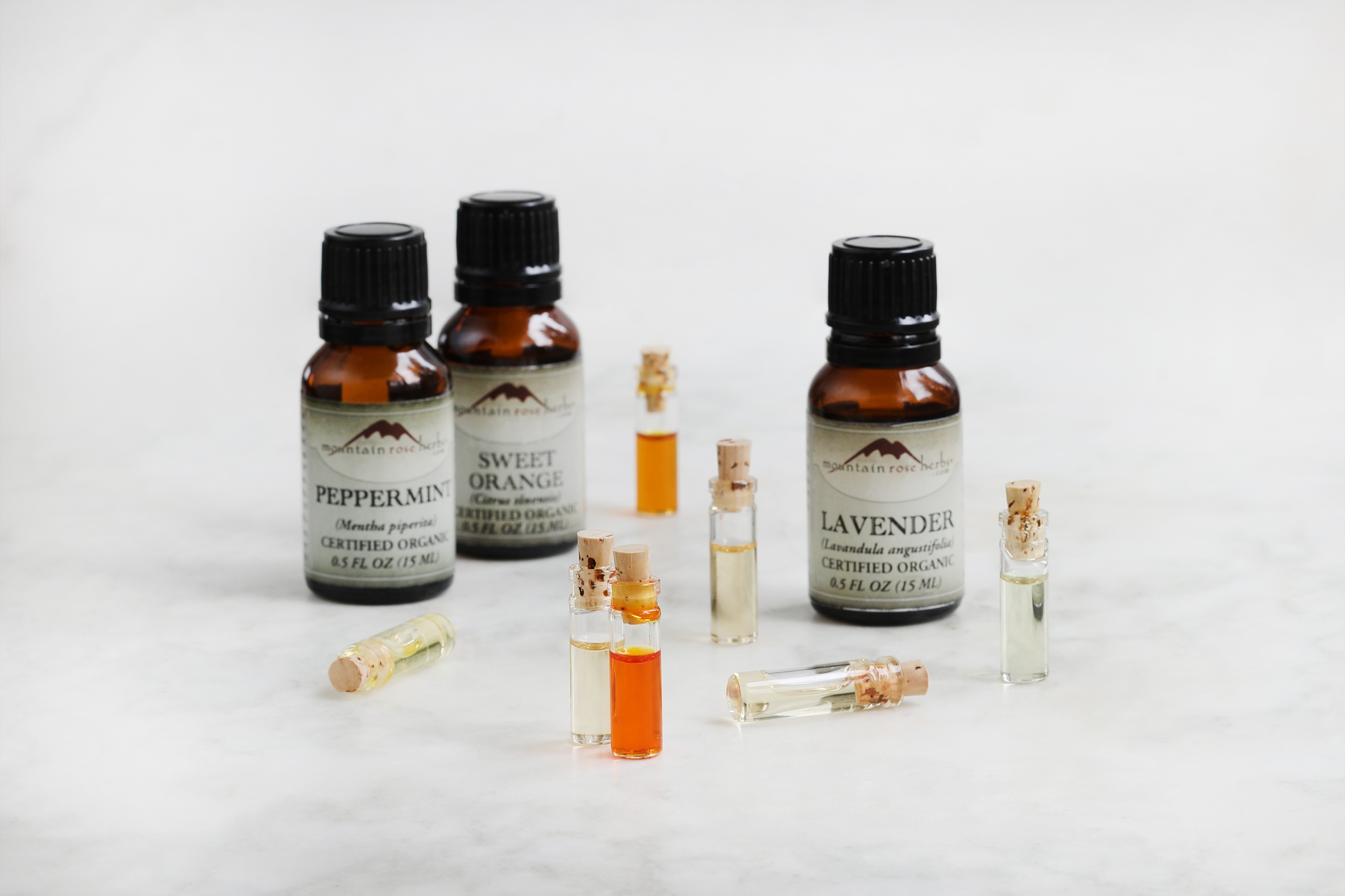 Amber bottles and small clear corked vials of essential oils on marble counter.