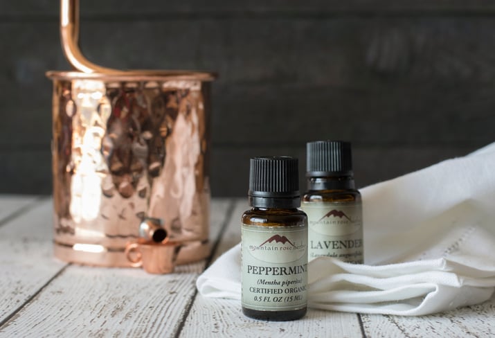 Small bottle of peppermint essential oil sitting next to a copper still on a wooden table
