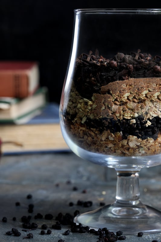 Snifter glass filled with dried berries and spices with books in background