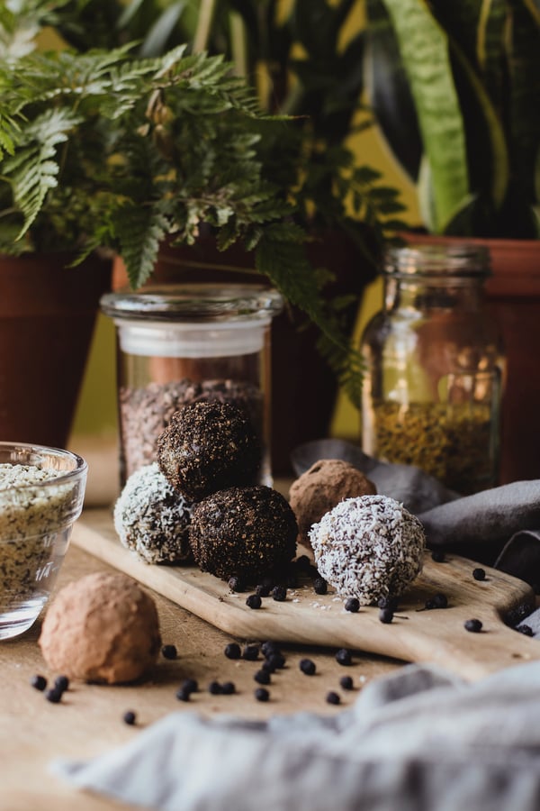 Protein Energy Balls rolled in cocoa and coconut laid out on a cutting board amidst hemp seeds, cacao and other ingredients.