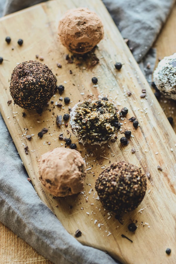 Five protein and energy balls rolled in a variety of herbal powders on a cutting board.