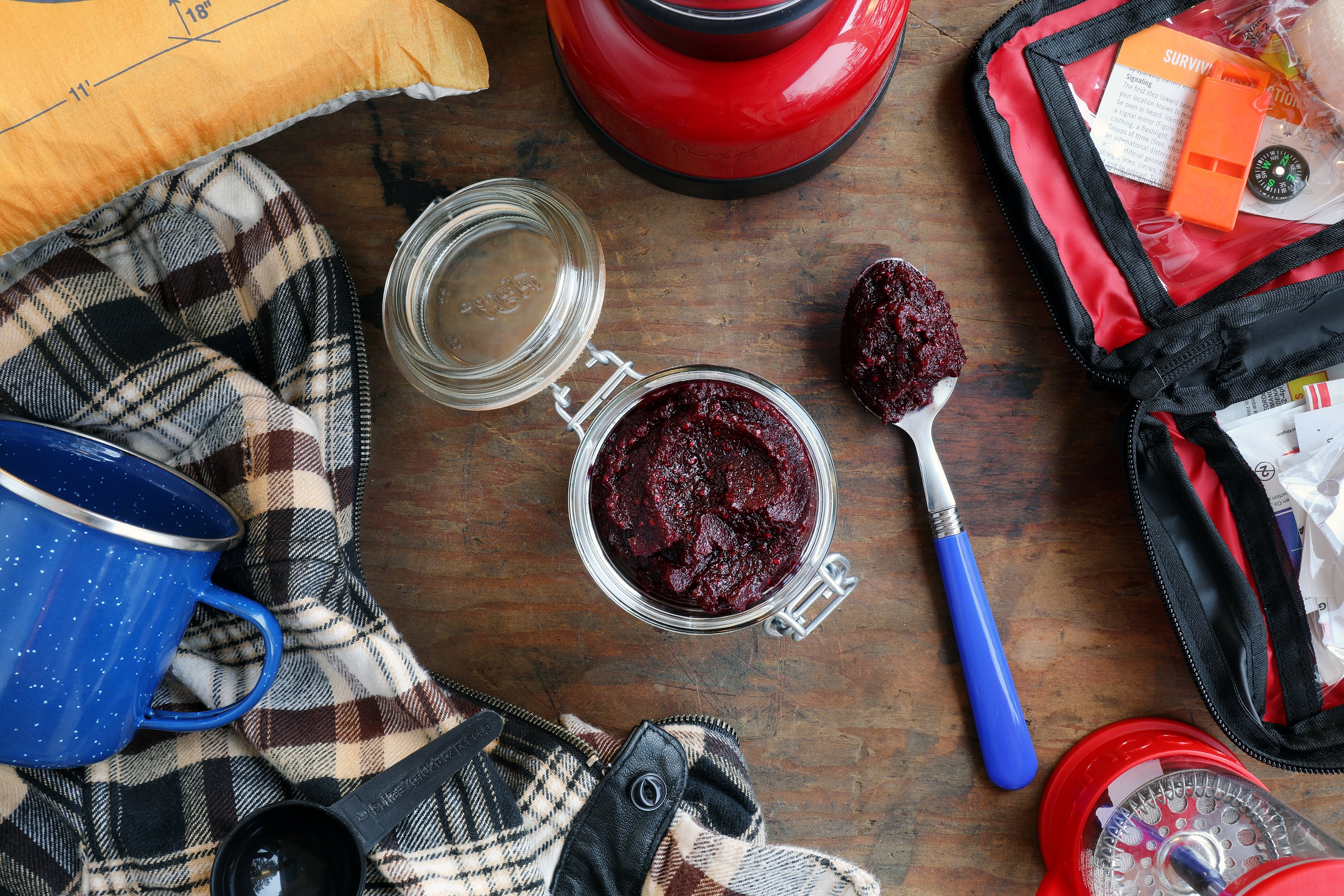 Clamp jar with deep red paste surrounded by camping gear and accessories.