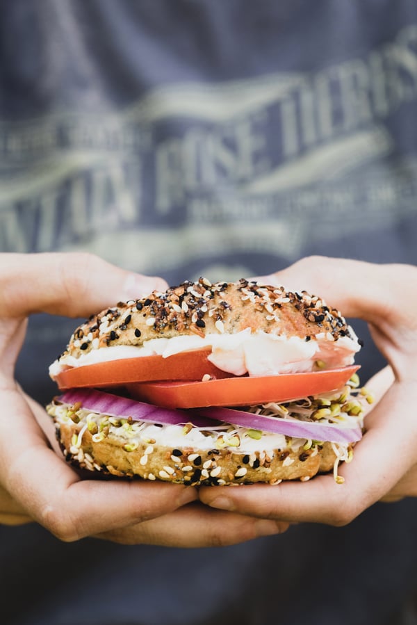 Hands holding an everything bagel sandwich.