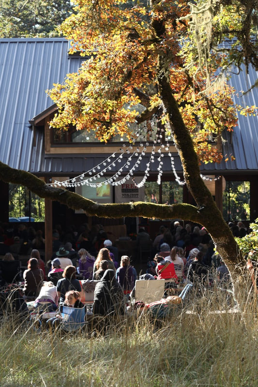 People sitting near grass, gathered behind open arboretum listening to a lecture