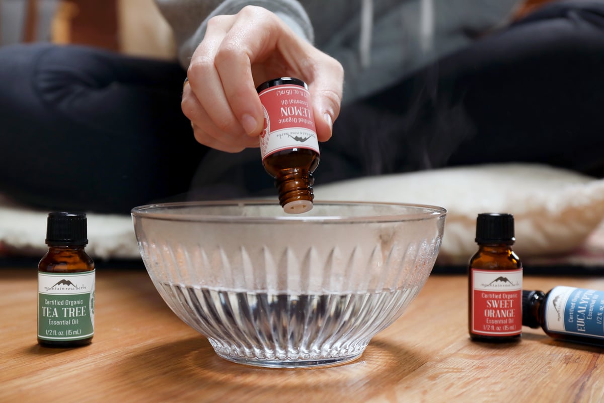 Hand adding drops of lemon eucalyptus essential oil to bowl of water for facial steam.