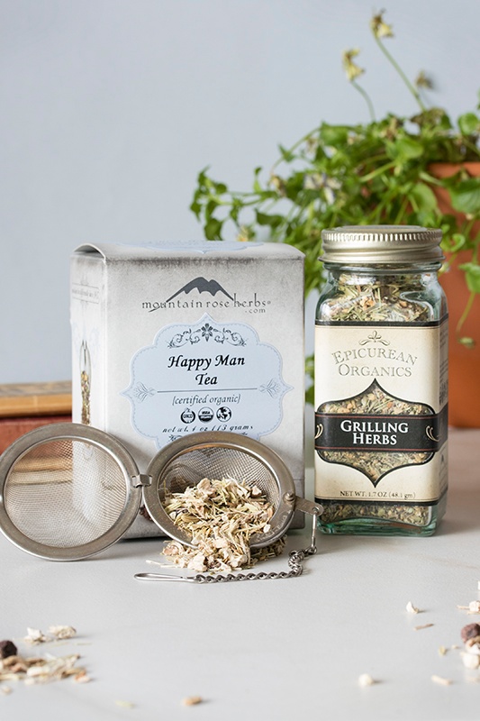 Box of happy man tea, bottle of grilling herbs, and tea infuser with loose-leaf tea
