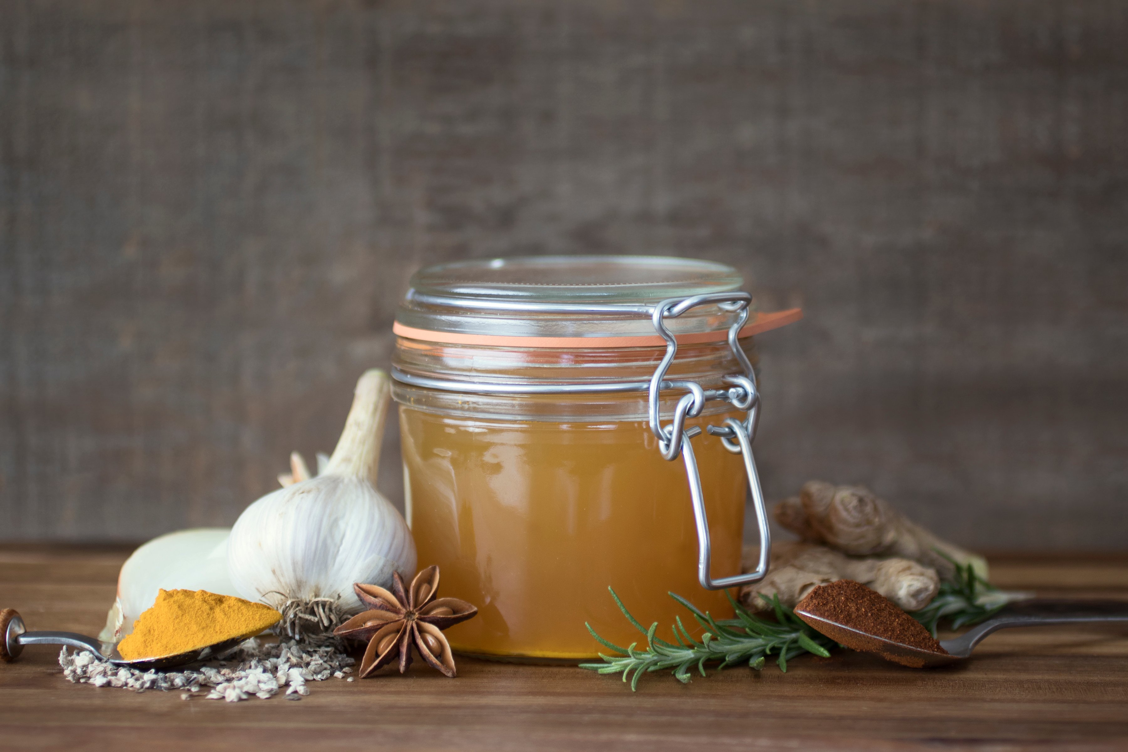 Homemade fire cider in a glass pantry jar is a deep yellow color and features organic herbs and spices like garlic, anise star pod, turmeric powder, rosemary, ginger root, and more. 