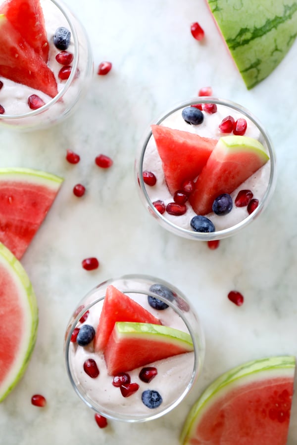 Vegan whipped coconut cream in pretty dishes with watermelon, pomegranate seeds and blueberries.