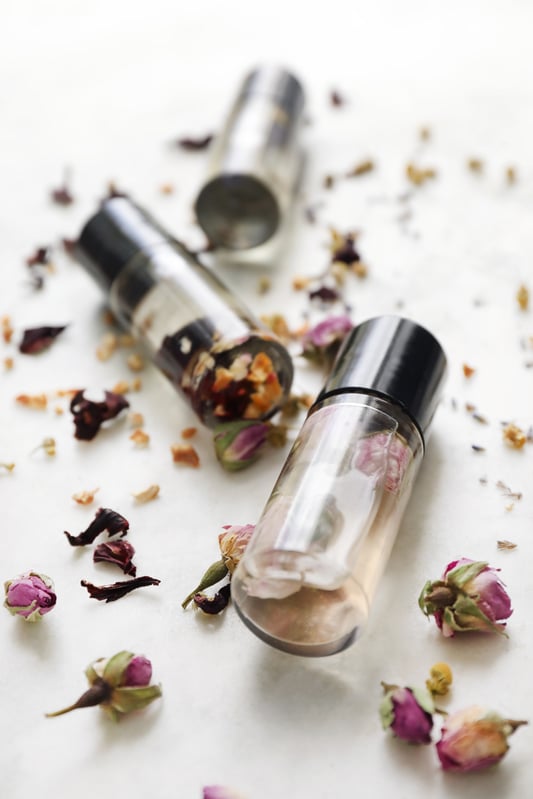 Clear perfume bottles with real flowers inside surrounded by more dried flowers. 