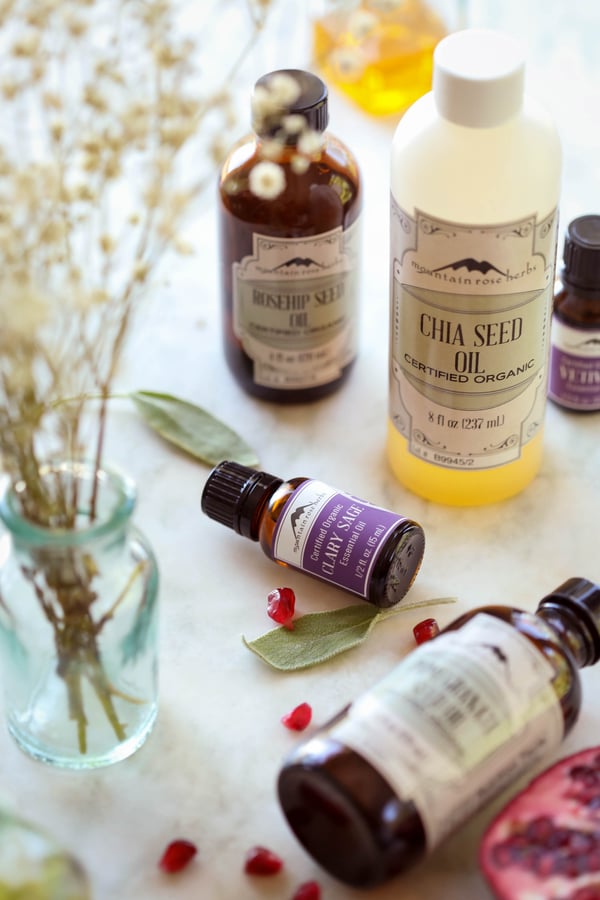 Ingredients on a table to make DIY foaming hand and body soap recipe, including rosehip seed oil, chia seed oil, pomegranate seed oil and clary sage and vetiver essential oils.