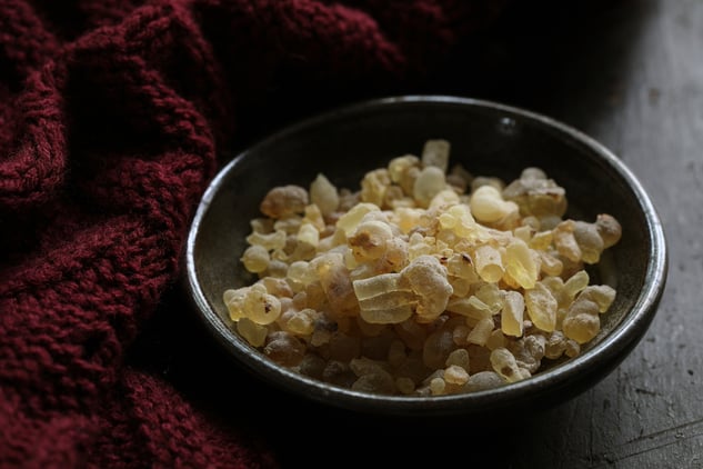 frankincense tears in a dark bowl next to a red knit scarf