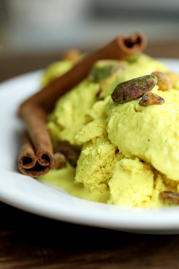 Vegan golden milk coconut ice cream on a dish garnished with pistachios and cinnamon sticks.