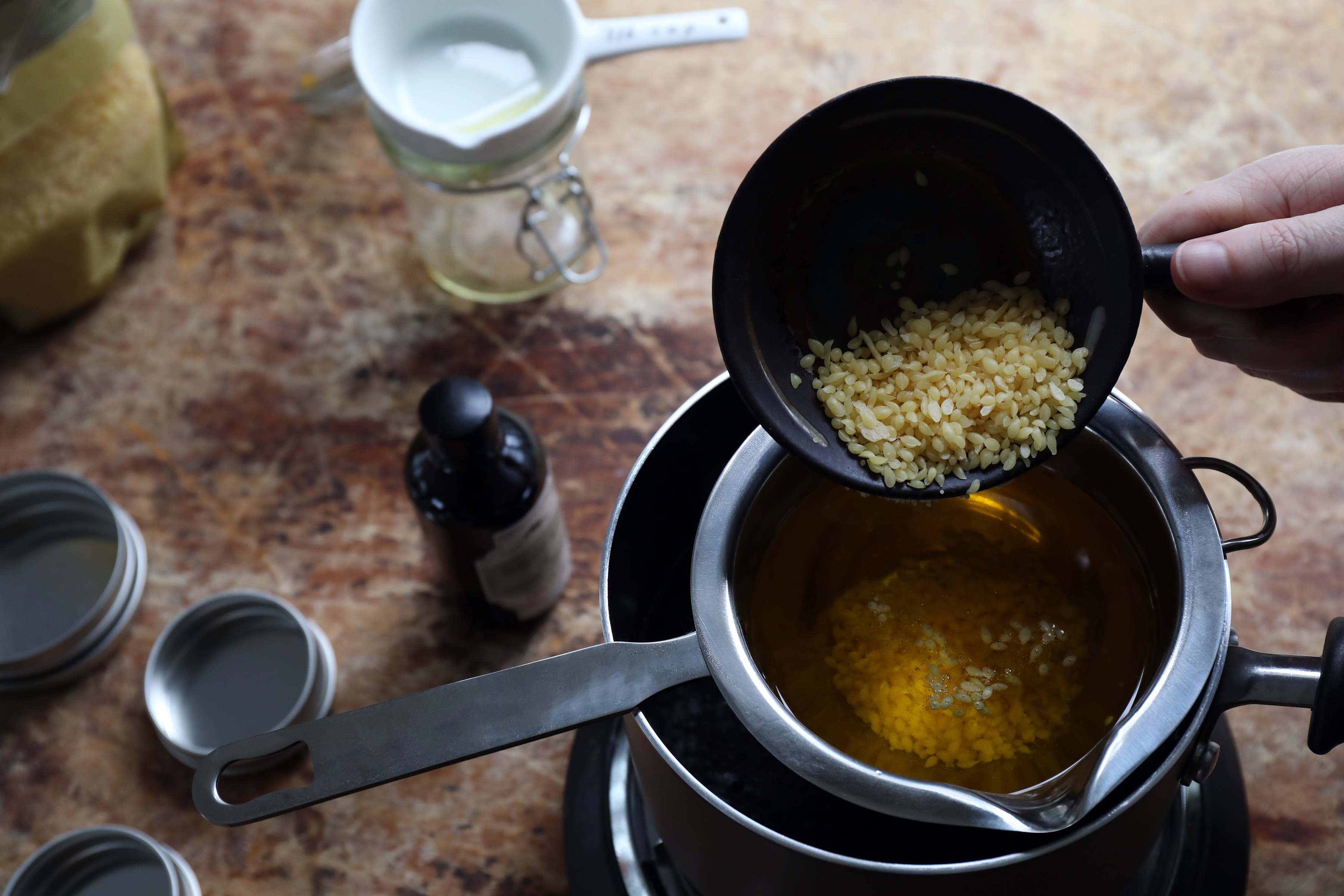 Pouring beeswax and oil into a double boiler. 