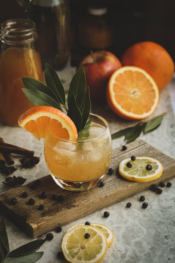 Sparkling herbal gin fizz on a board with bay leaves garnish and an orange twist