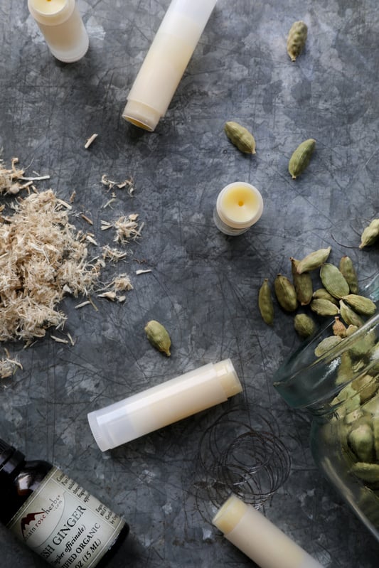 Filled lip balm tubes with botanicals and essential oils displayed around on a rustic metal table.