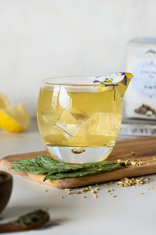 Clear glass of ginger palmer mocktail with ice cubes with lemon wedges and ginseng