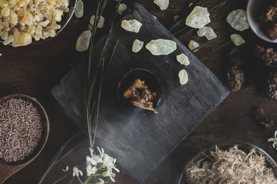 A variety of gums and resins laid out on a table with herbs and flowers.