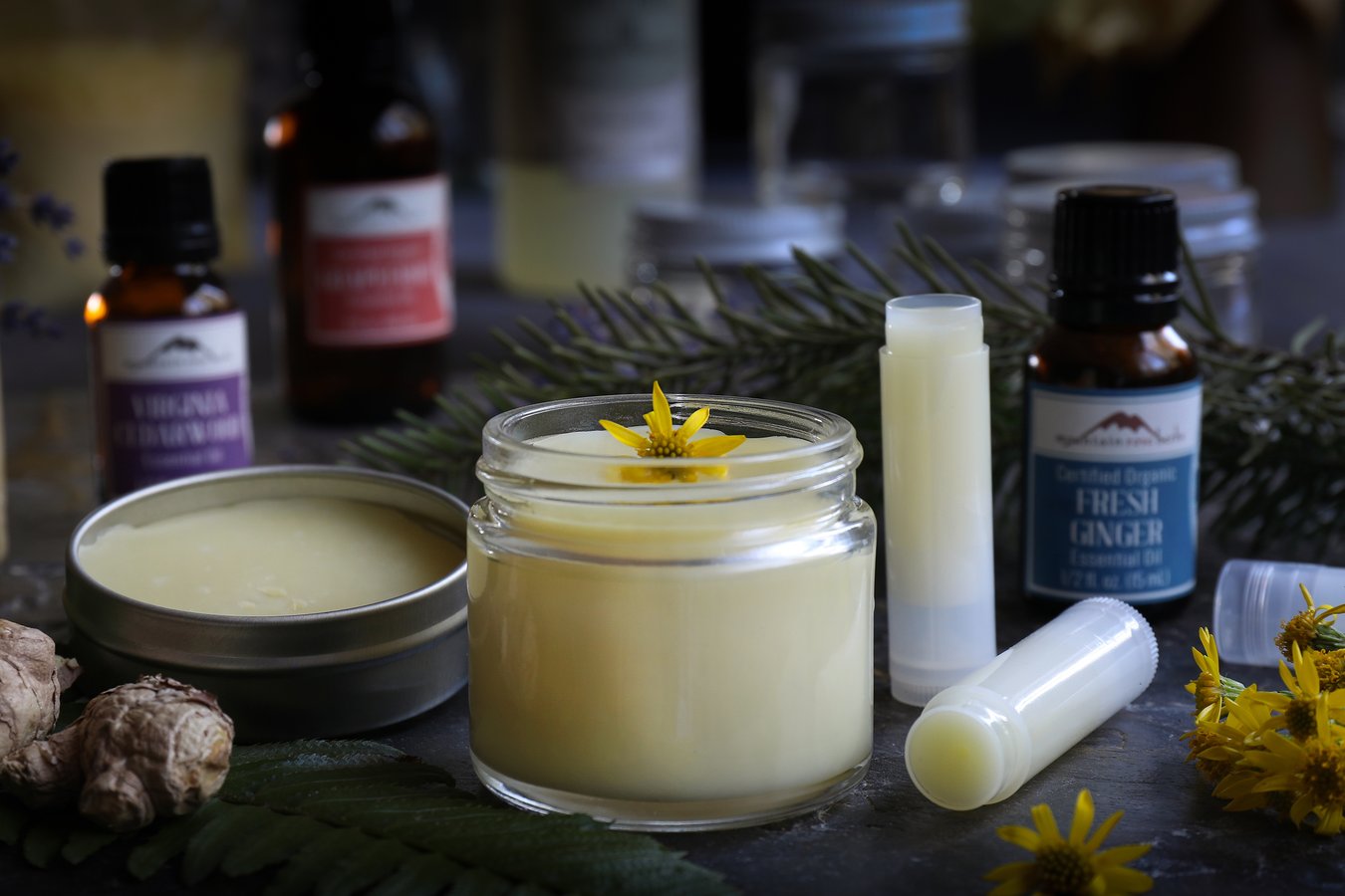DIY Solid perfume in a tin, a jar, and a tube surrounded by pure essential oils.