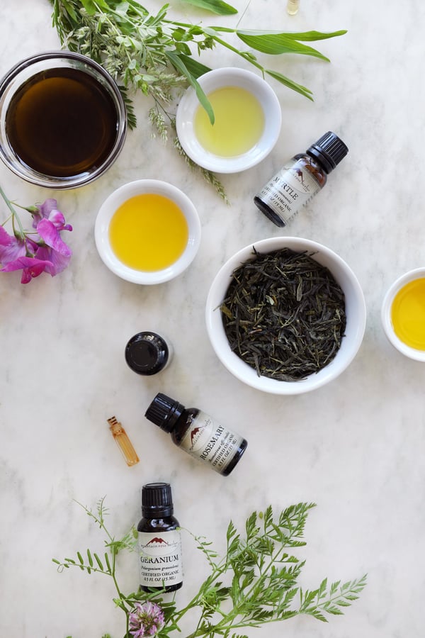 Ingredients are arranged in bowls for a green tea serum including a green tea herbal oil, various essential oils, and dried green tea leaves.