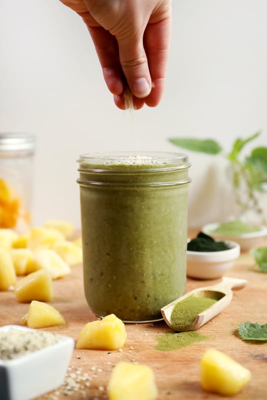 Green super smoothie in canning jar glass being sprinkled with hemp seeds.