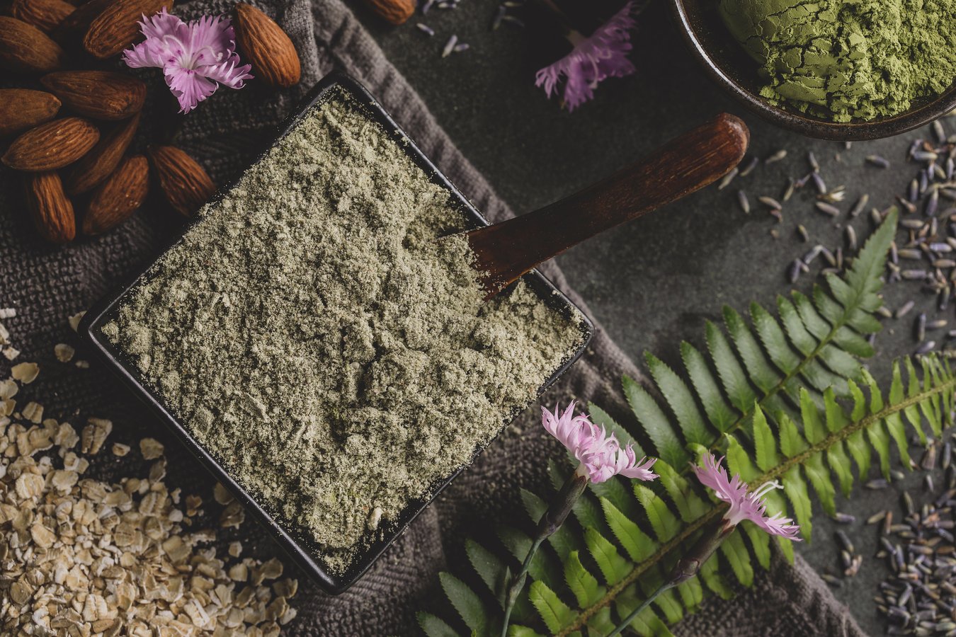 Matcha and lavender cleansing grains surrounded by almonds, oatmeal and lush ferns.