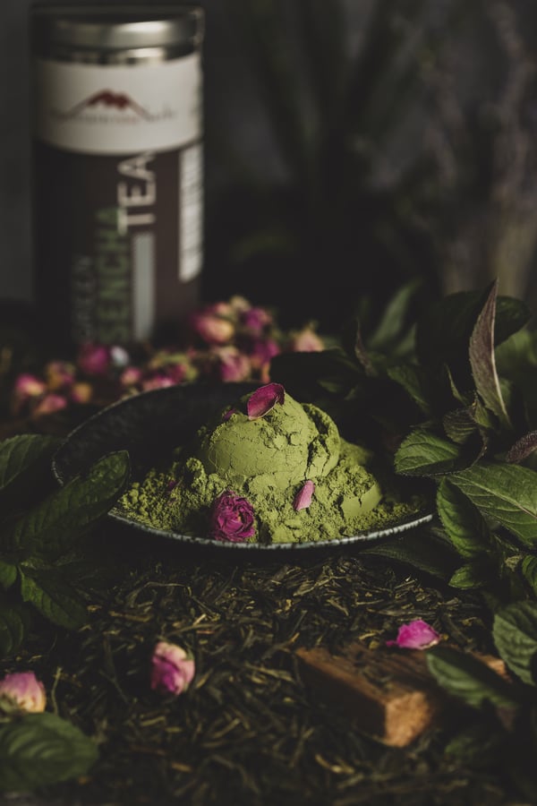 Vibrant matcha green tea in a bowl surrounded by beautiful rose petals.
