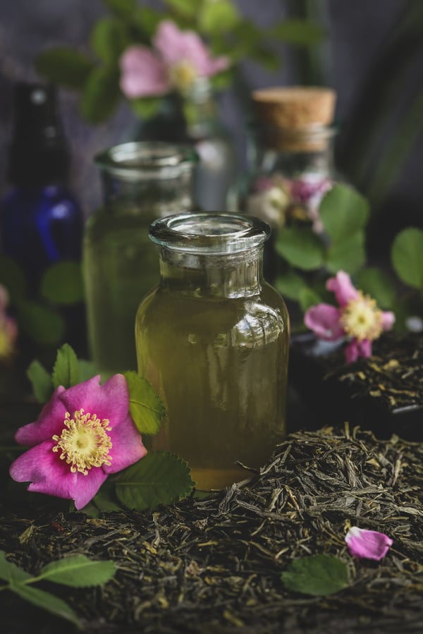 Green tea and rose toner in a glass jar surrounded by green sencha tea and flowers.
