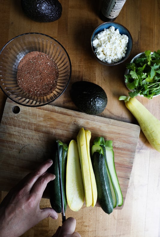 Hand slicing long yellow squash and zucchini to make slices for grilling with adobo spice rub