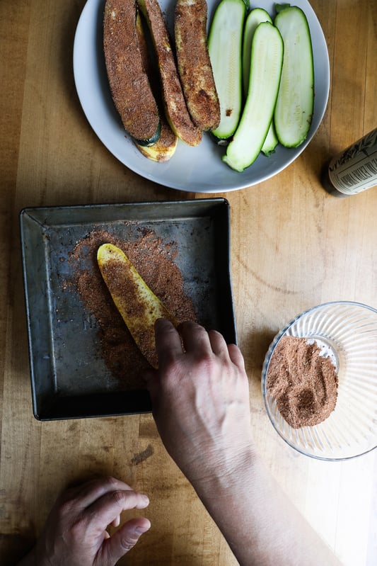 Hand placing squash slice onto a tray with adobo spice for marination and grilling