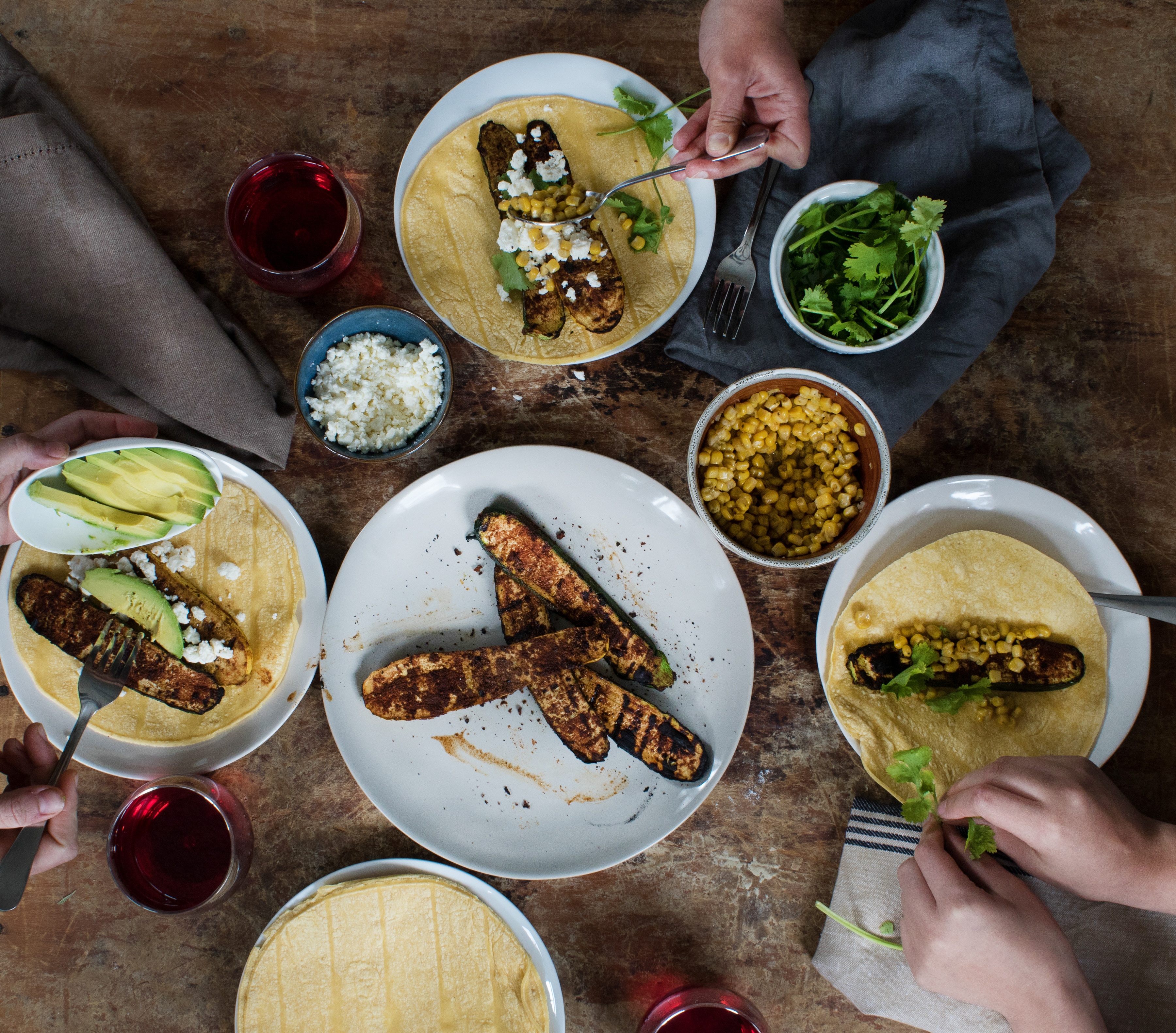 Plates, sides, and grilled veggies with adobo rub for group meal with hands eating and breaking cilantro