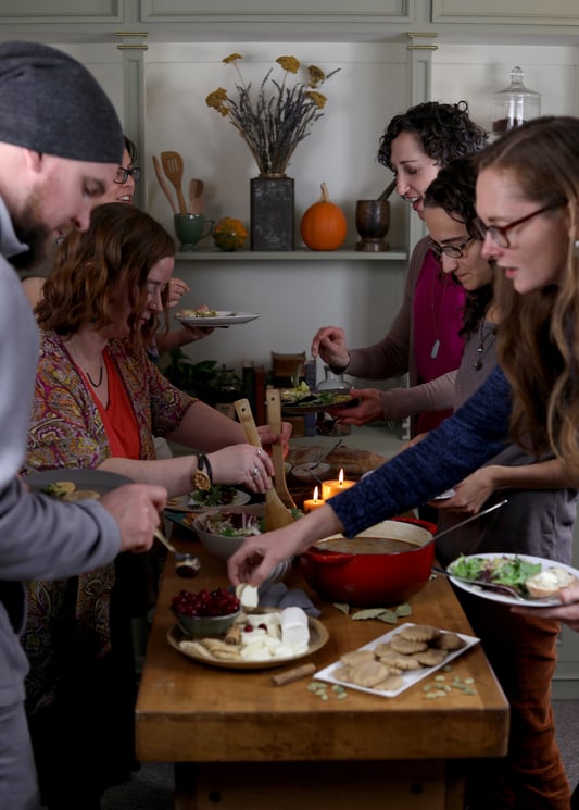 Mountain Rose Herbs employees gathered around a wood table full of potluck dishes including cookies salad and cranberries