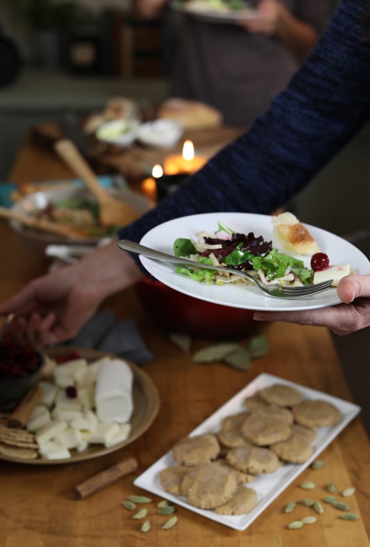 Hand holding fresh salad, reaching for cranberries  and cheese, hovering over group meal table
