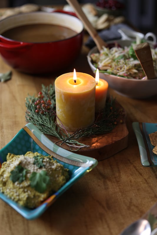 Beeswax candle in the middle of a table by fir wreath as decoration for group meal potluck during holiday