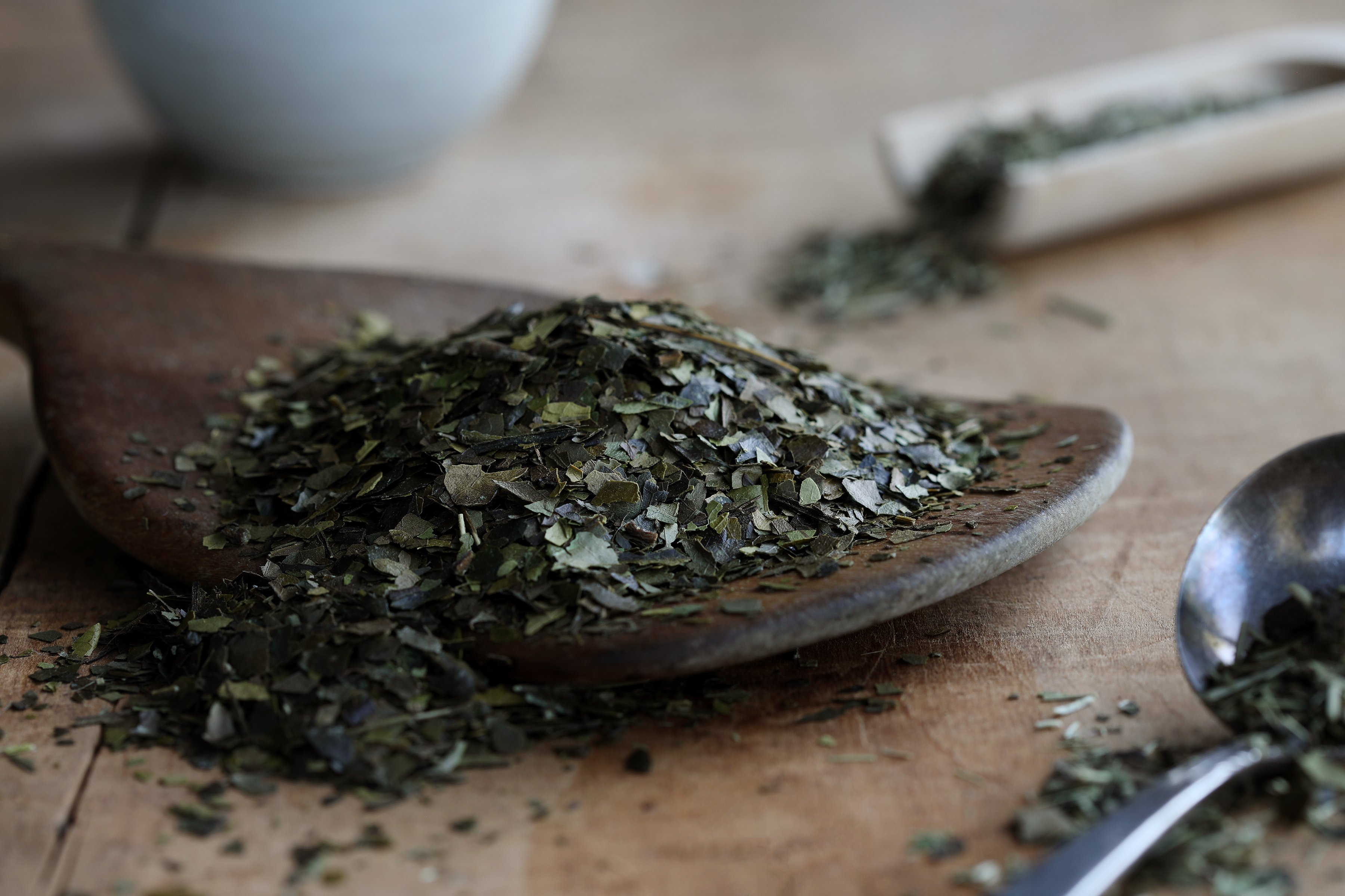 Spoon of green botanicals spilling onto rustic wooden table.