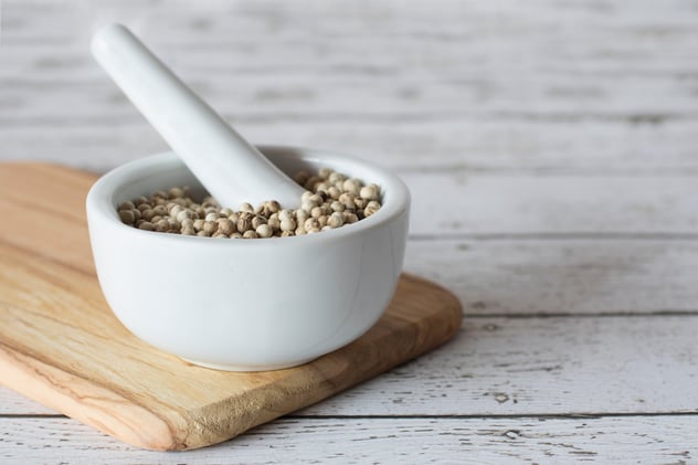 White peppercorns in a mortar on top of a chopping board with a pestle