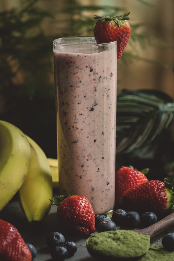 Tall berry smoothie surrounded by fresh colorful fruit. 