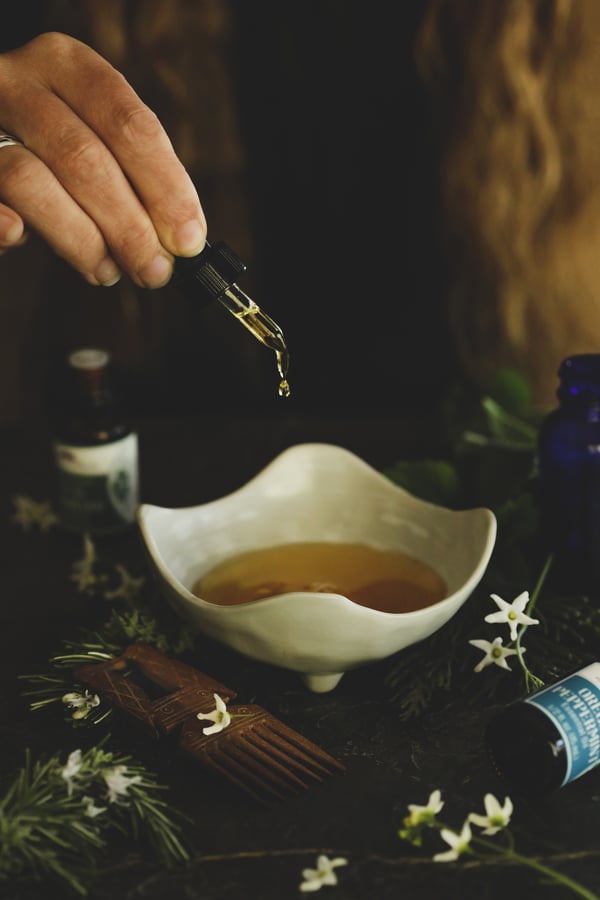 Unique white bowl with oil, surrounded by essential oils and a vintage hair comb. 