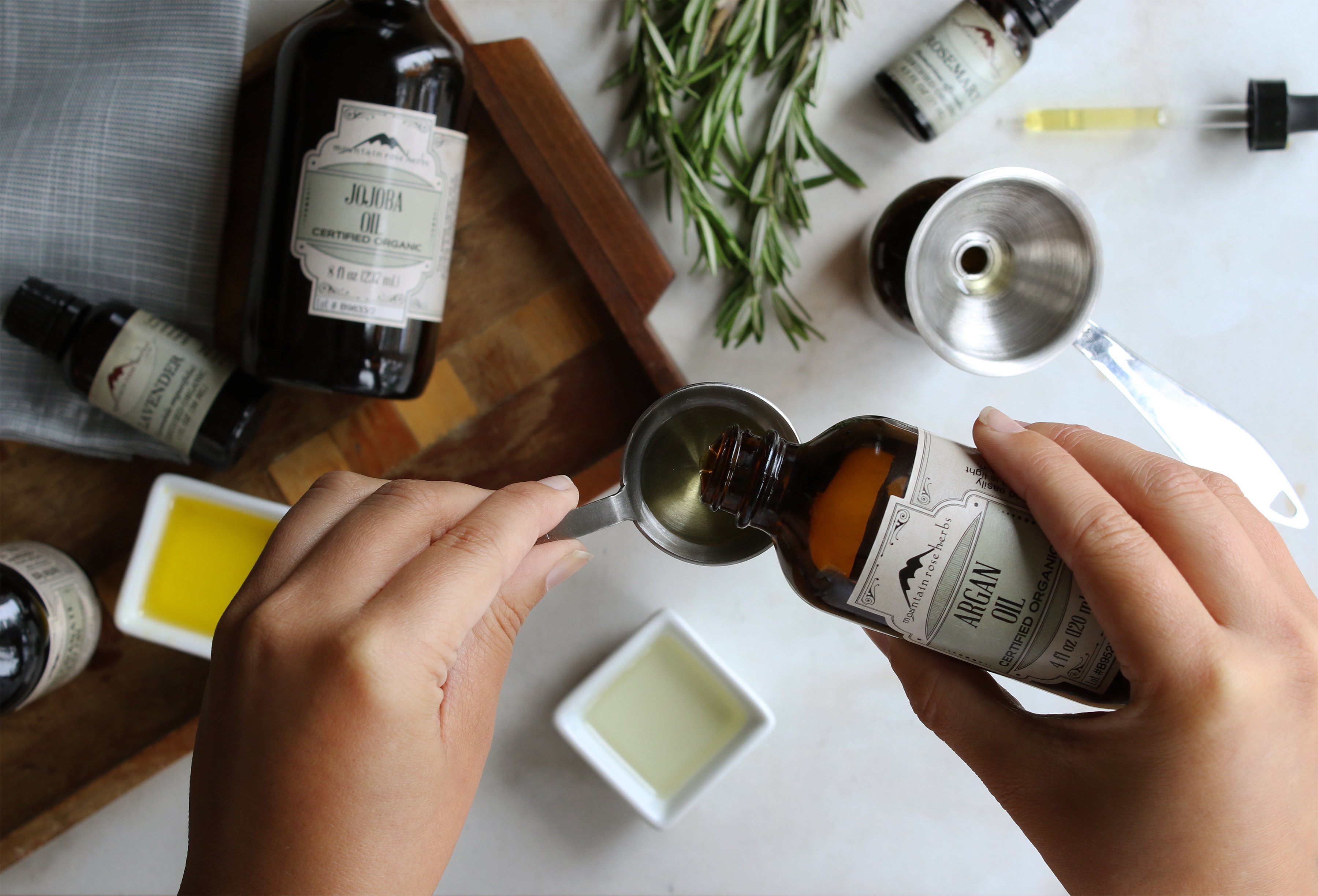 Preparing the ingredients for a DIY hair serum using organic argan oil, organic jojoba oil, and organic essential oils of rosemary and lavender.