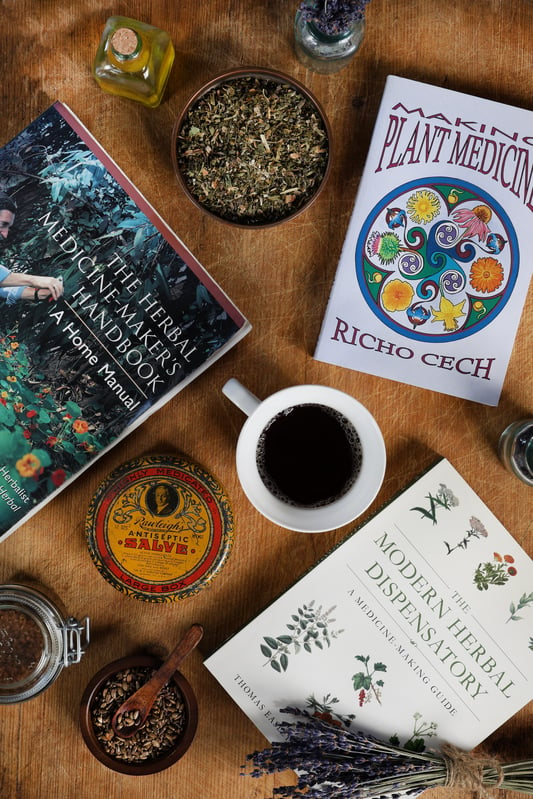 Several books about herbal medicine surrounded by herbs, a cup of tea and vintage props. 