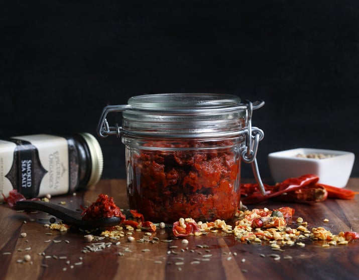 Pantry jar filled with red chili harissa paste sitting next to ingredients for the recipe